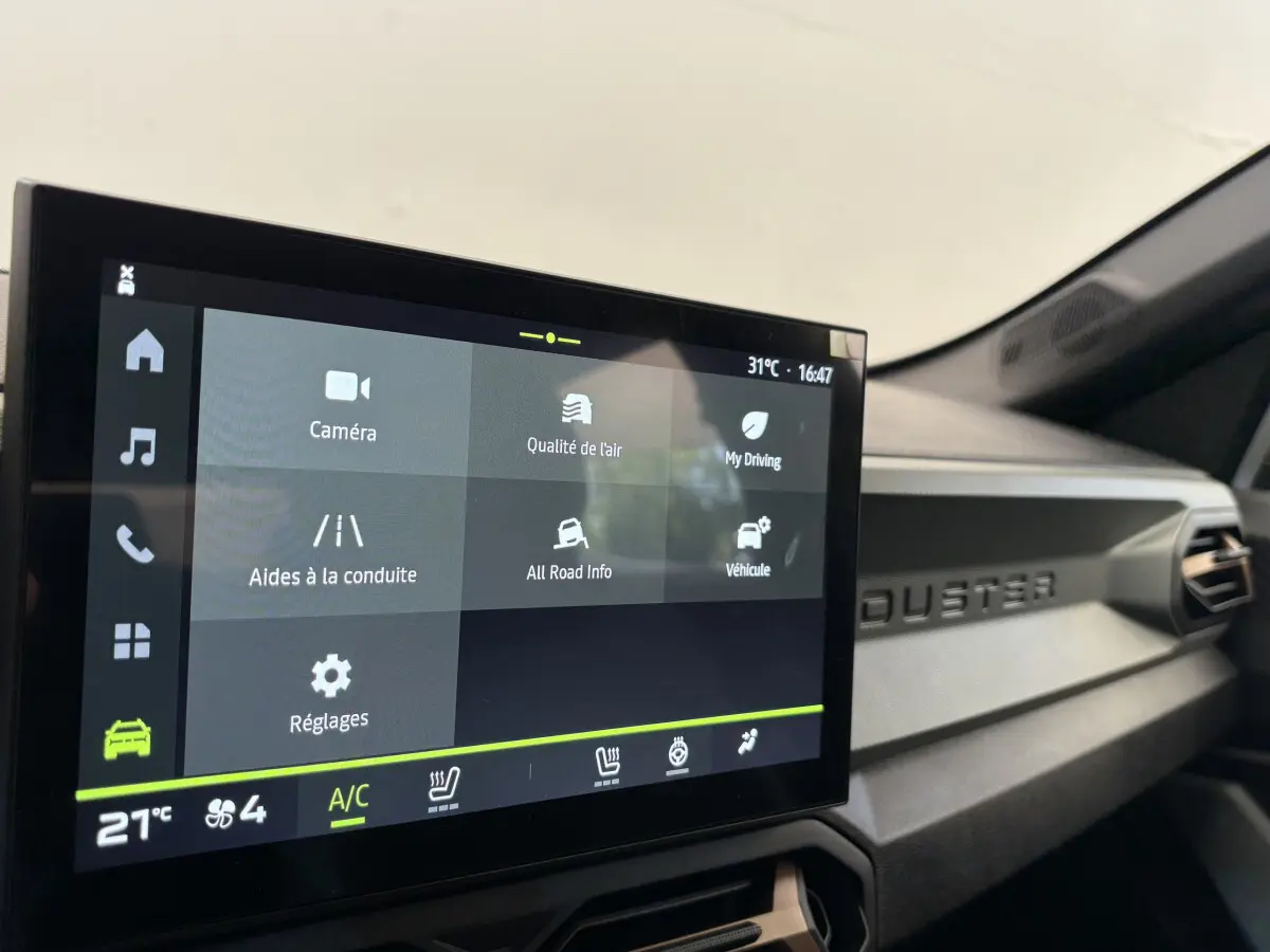 Écran tactile central affichant les aides à la conduite dans l'habitacle noir du Dacia Duster 2025 côté passager.