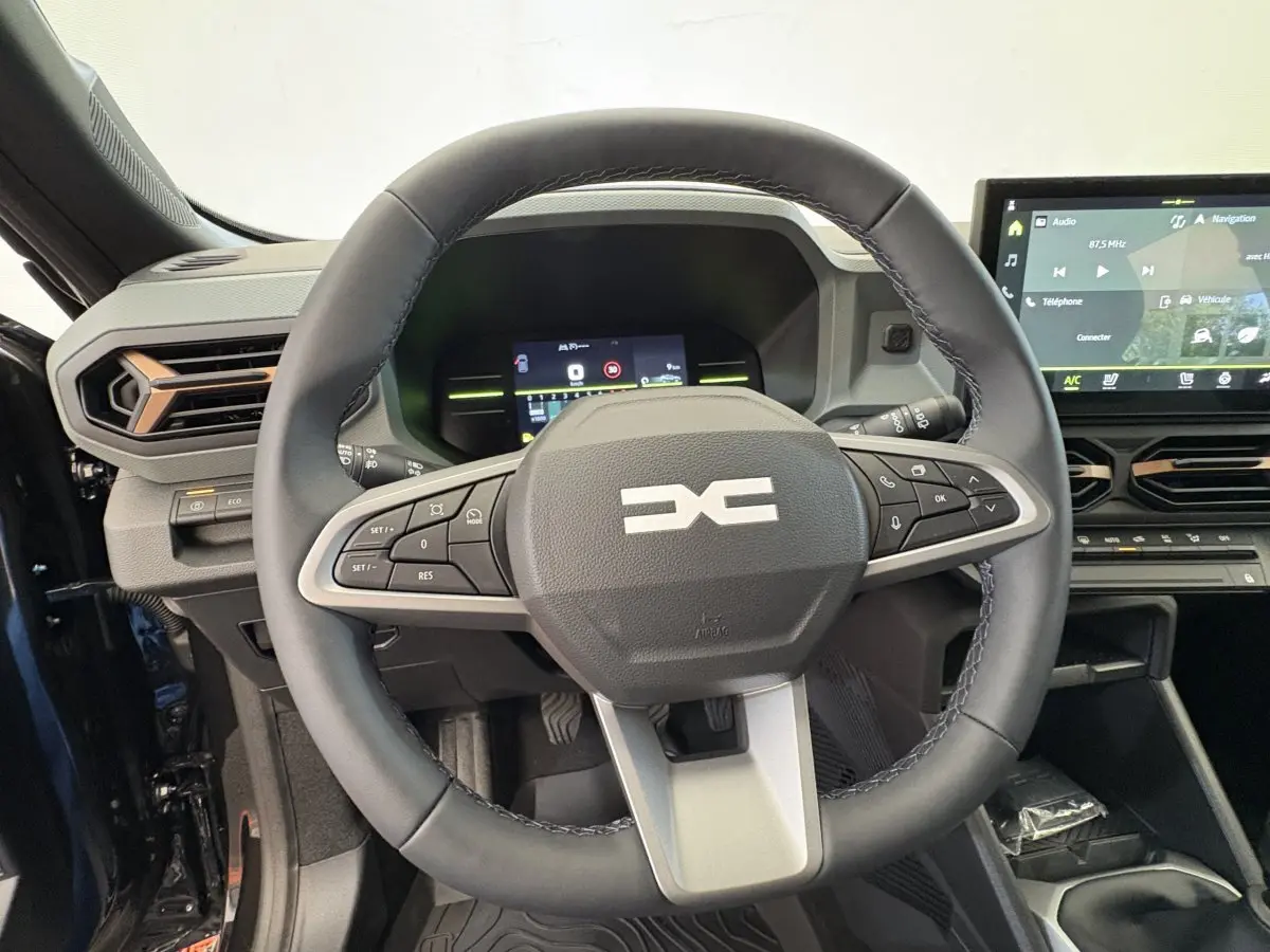 Vue intérieure centrée sur le volant cuir du Dacia Duster 2025 noir avec tableau de bord numérique et écran tactile.