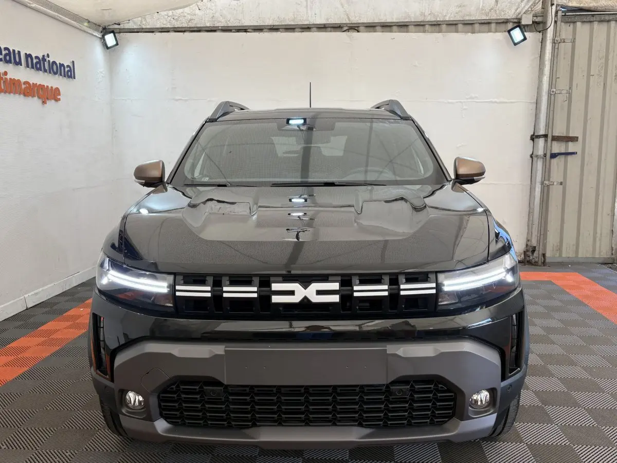 Vue frontale d'un Dacia Duster noir 2025 avec phares LED allumés et calandre marquée du logo DACIA.