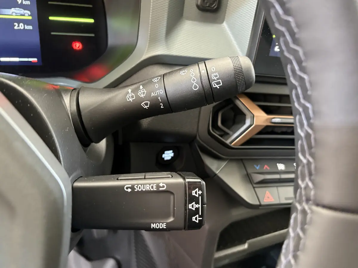 Gros plan sur la commande multifonction et le commodo d’essuie-glace du tableau de bord du Dacia Duster noir 2025.