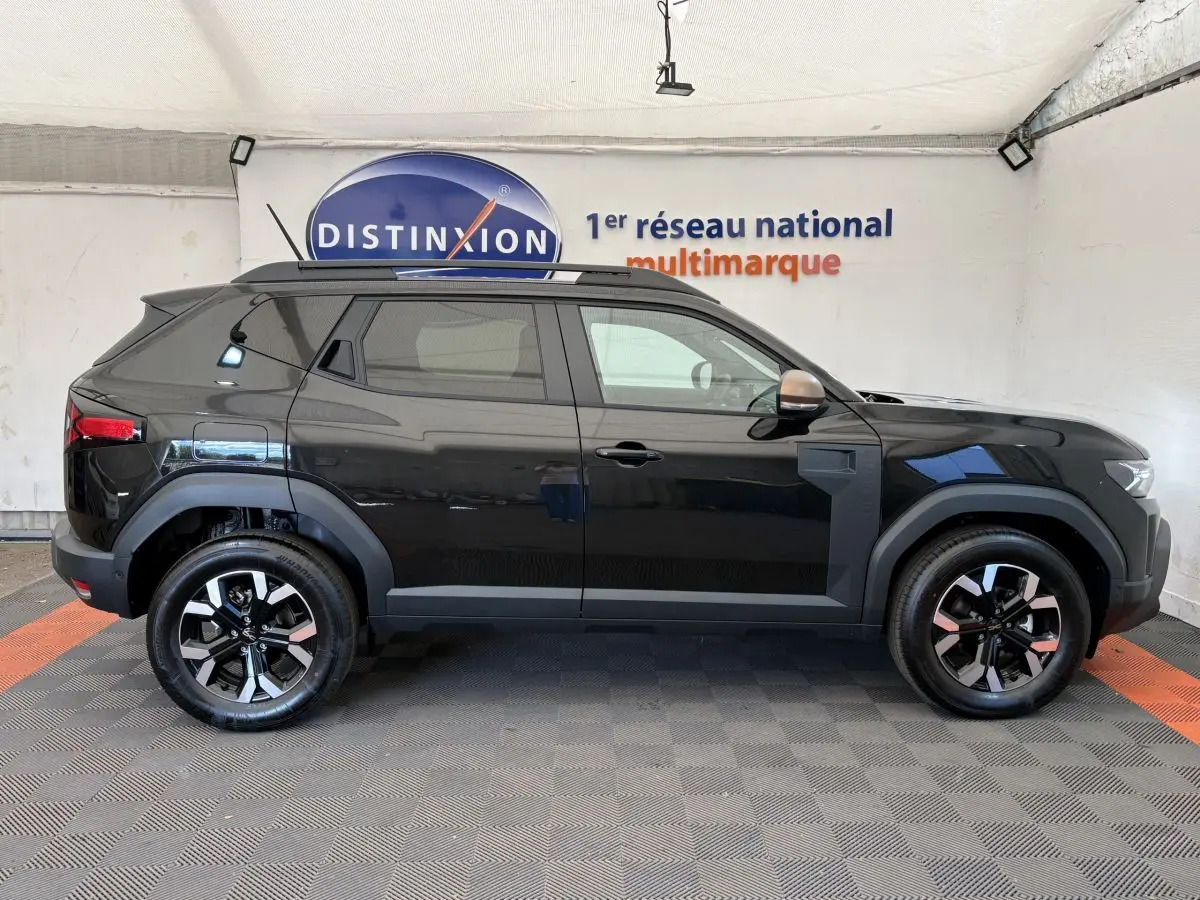 Profil droit du Dacia Duster noir 2025 avec jantes alliage et barres de toit noires en intérieur showroom.