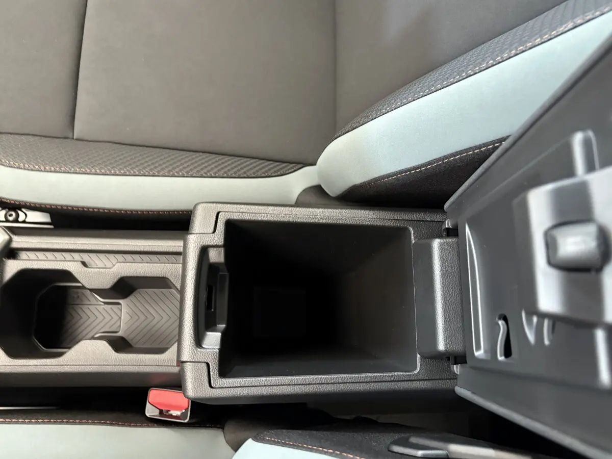 Gros plan sur la console centrale ouverte du Dacia Duster noir 2025, montrant le rangement intérieur et les surpiqûres orange des sièges.