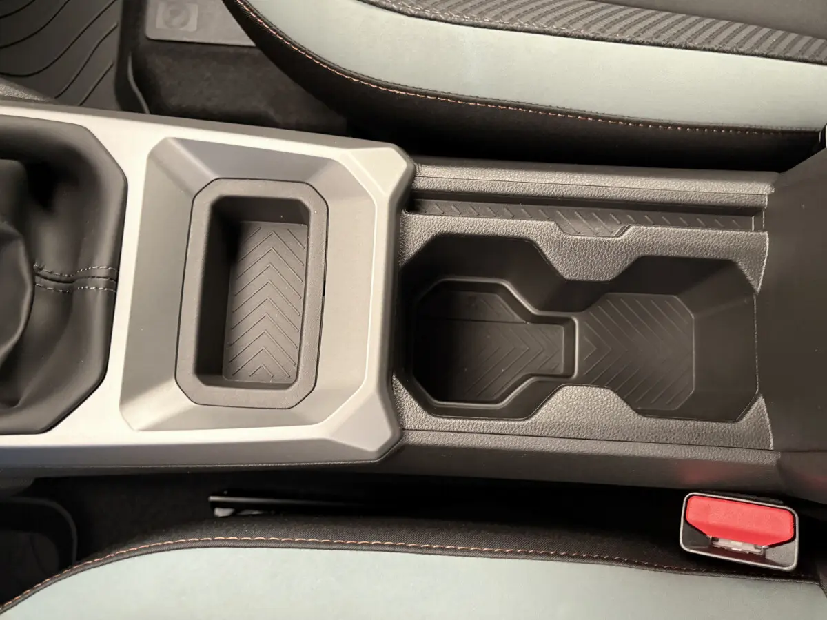 Gros plan sur la console centrale noire du Dacia Duster 2025 avec porte-gobelets et coutures orange visibles sur les sièges.