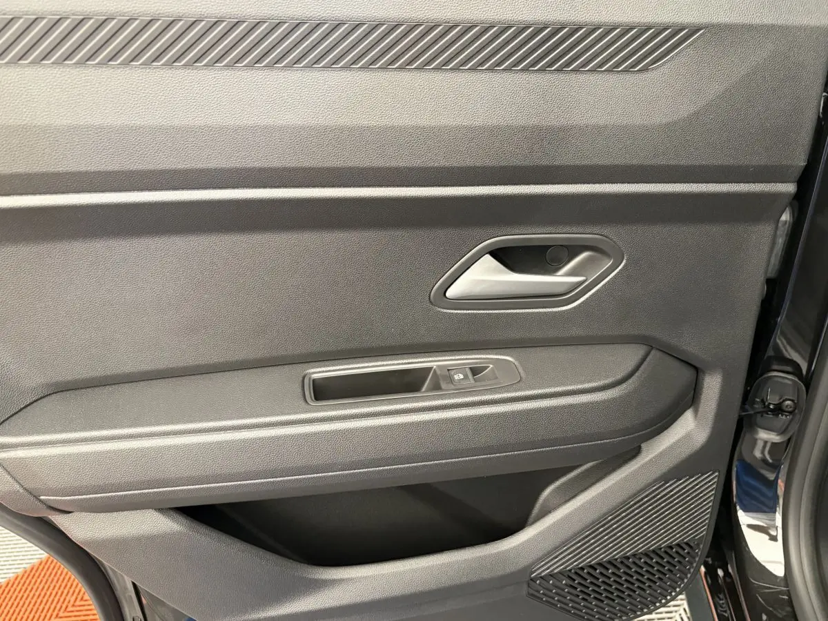 Intérieur côté gauche de la porte avant noire du Dacia Duster 2025 avec poignée et commande de vitre électrique.