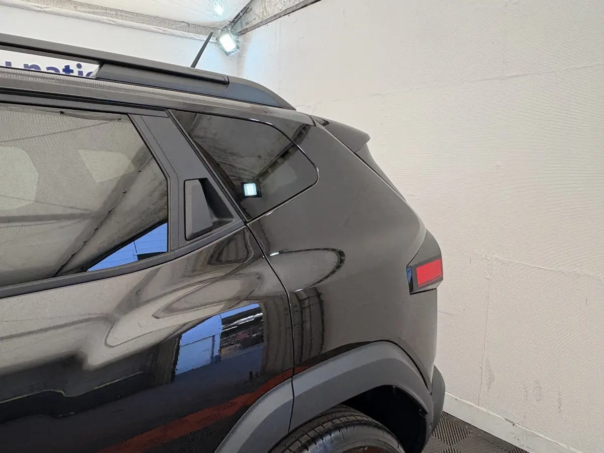 Vue arrière côté gauche du Dacia Duster noir 2025 avec barres de toit et feux arrière LED distinctifs.