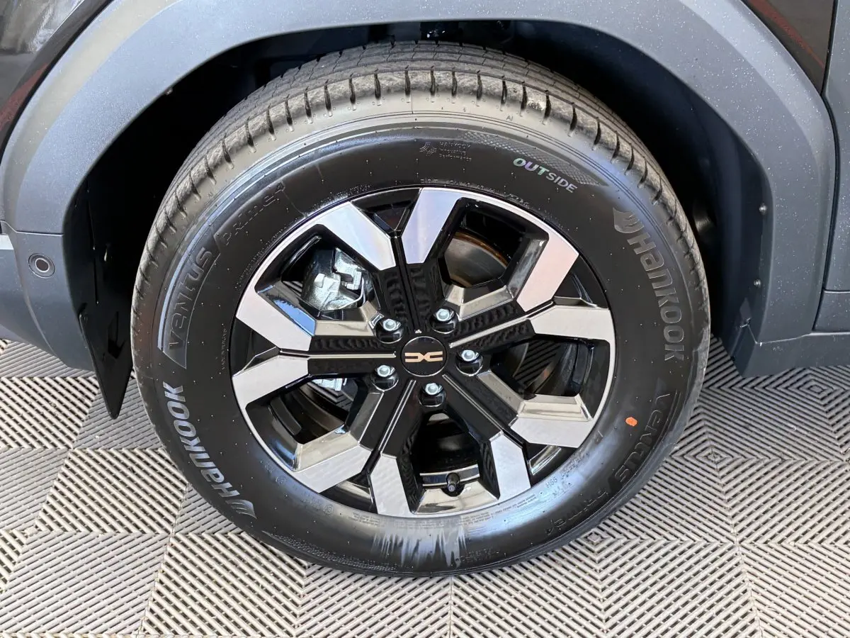 Gros plan sur la roue avant gauche noire du Dacia Duster 2025 avec jante alliage bicolore et logo central.