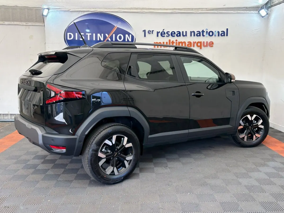 Dacia Duster noir vue de profil côté gauche, avec jantes alliage et barres de toit noires dans un showroom.