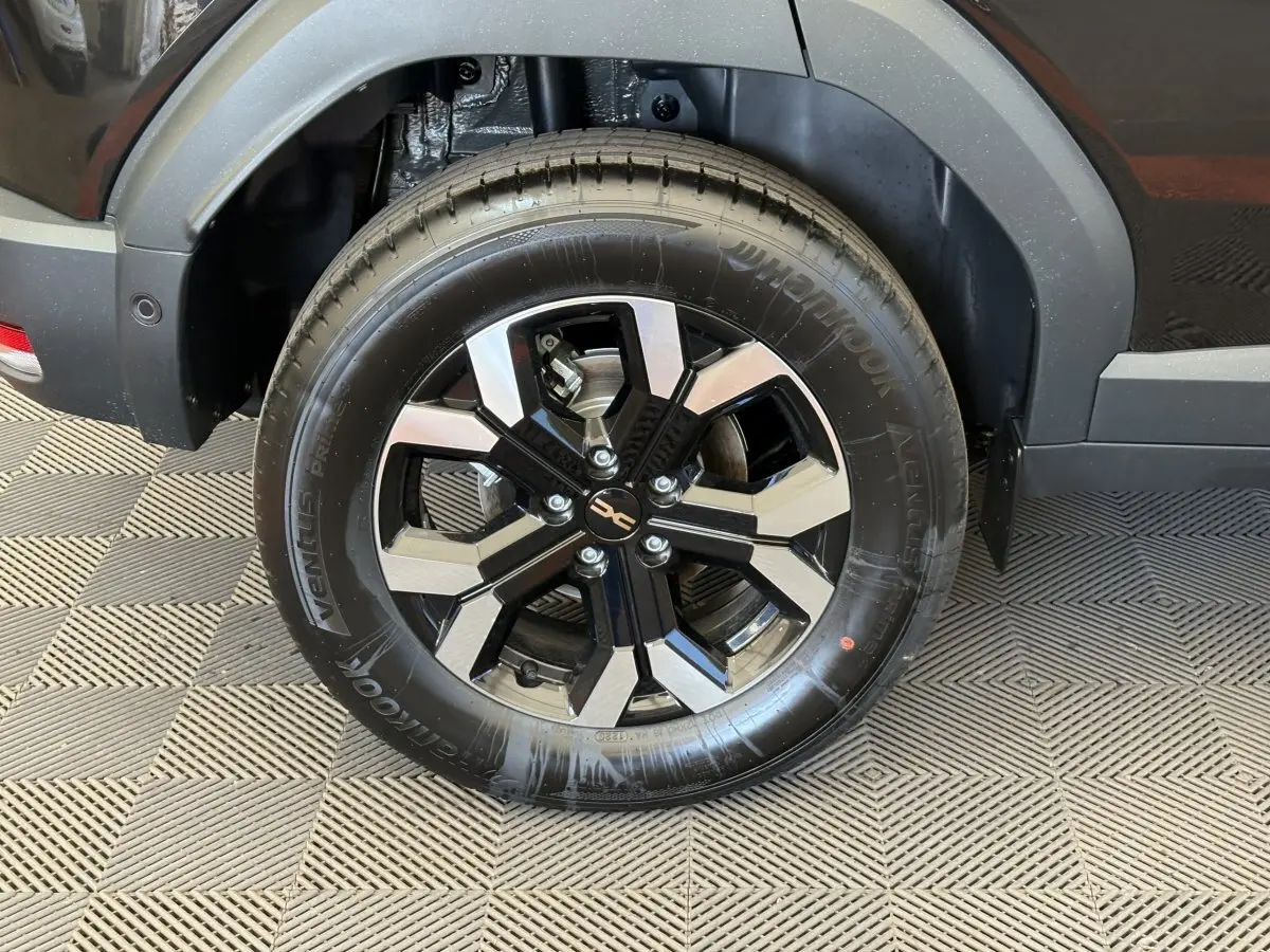 Gros plan sur la roue arrière droite du Dacia Duster noir 2025 avec jante alliage bicolore et pneu Hankook.