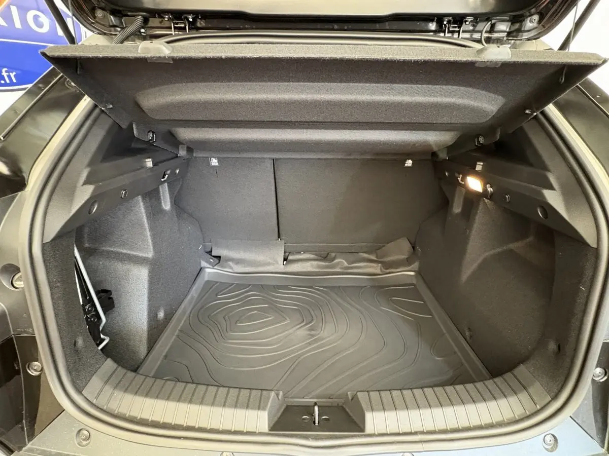 Coffre ouvert noir du Dacia Duster 2025 hybride, vue intérieure montrant tapis de protection et éclairage latéral.