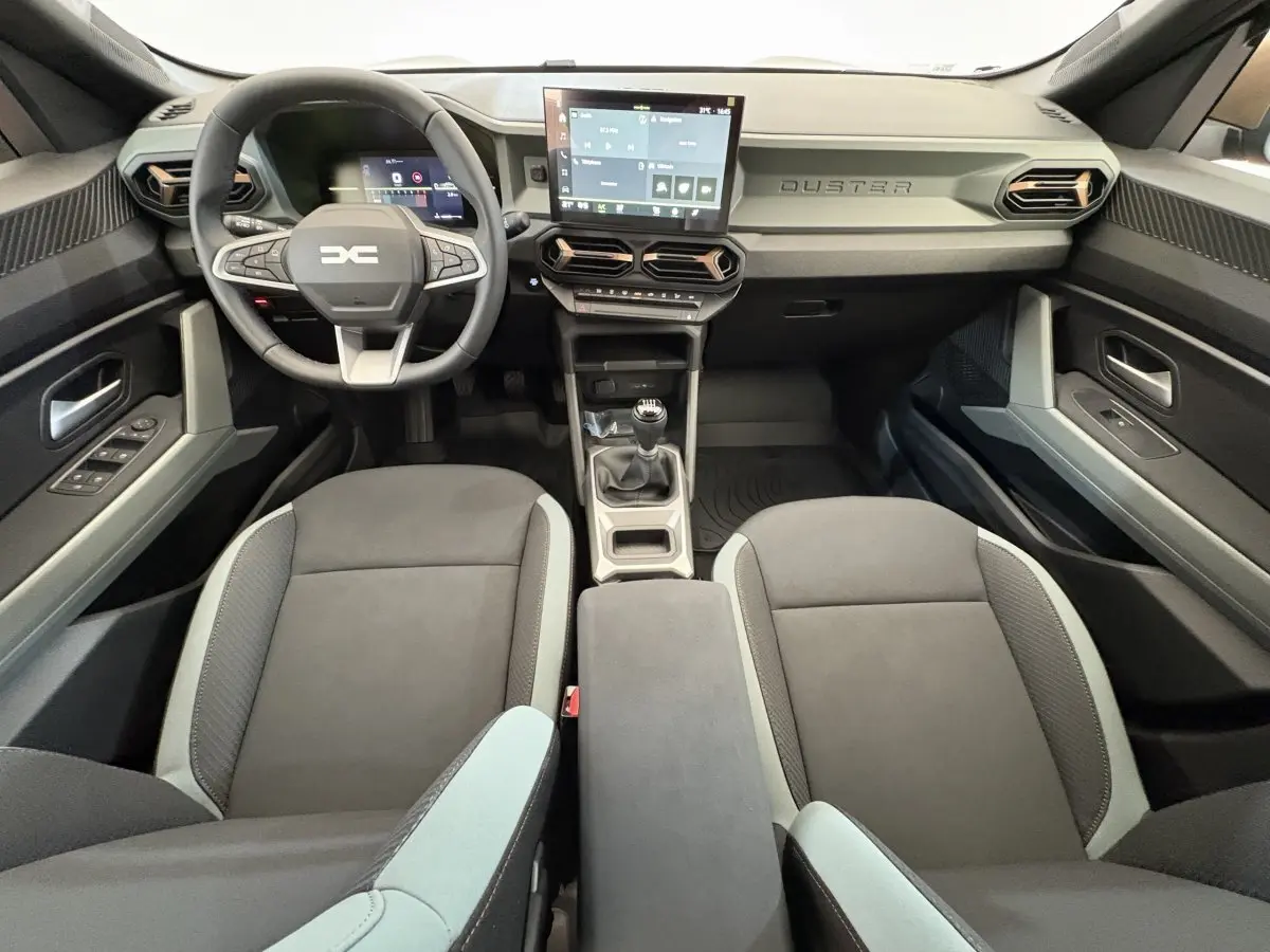 Intérieur du Dacia Duster 2025 noir, vue avant centrée sur le volant, tableau de bord et écran tactile.