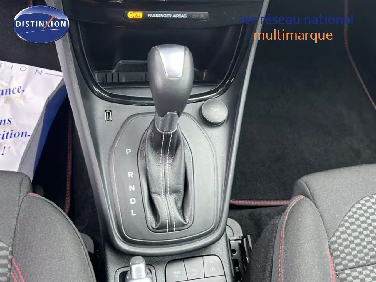 Le levier de vitesses automatique en cuir noir du Ford Puma 2024, avec console centrale et sièges tissu gris à surpiqûres rouges.