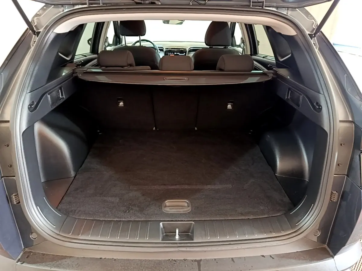 Coffre ouvert vu de l'arrière d'un Hyundai Tucson gris foncé, avec banquette arrière et cache-bagages visibles.