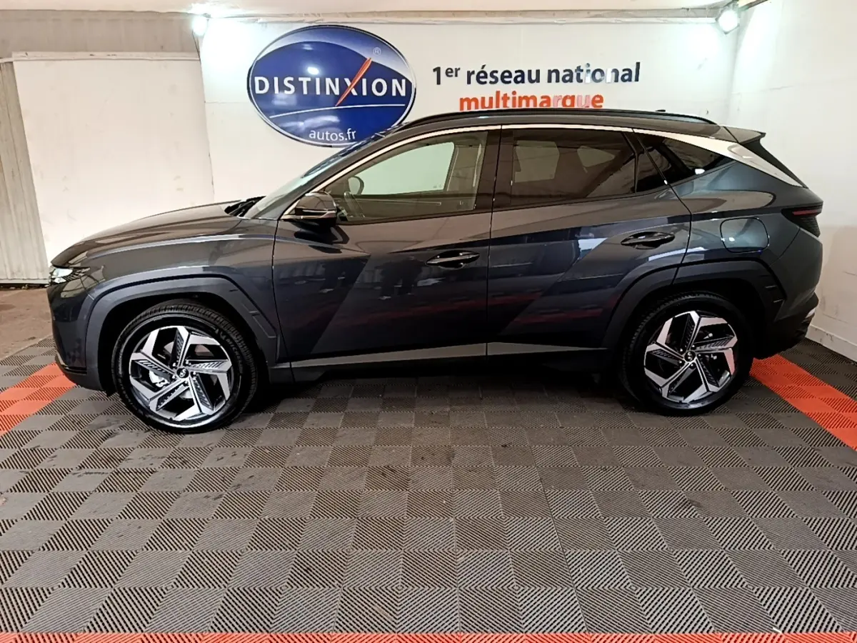 Vue de profil côté gauche d'un Hyundai Tucson gris foncé 2022 avec jantes alliage et toit noir dans un showroom.