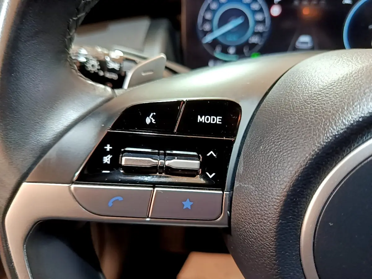 Gros plan sur les commandes gauche du volant cuir noir du Hyundai Tucson 2022, avec boutons mode et volume.