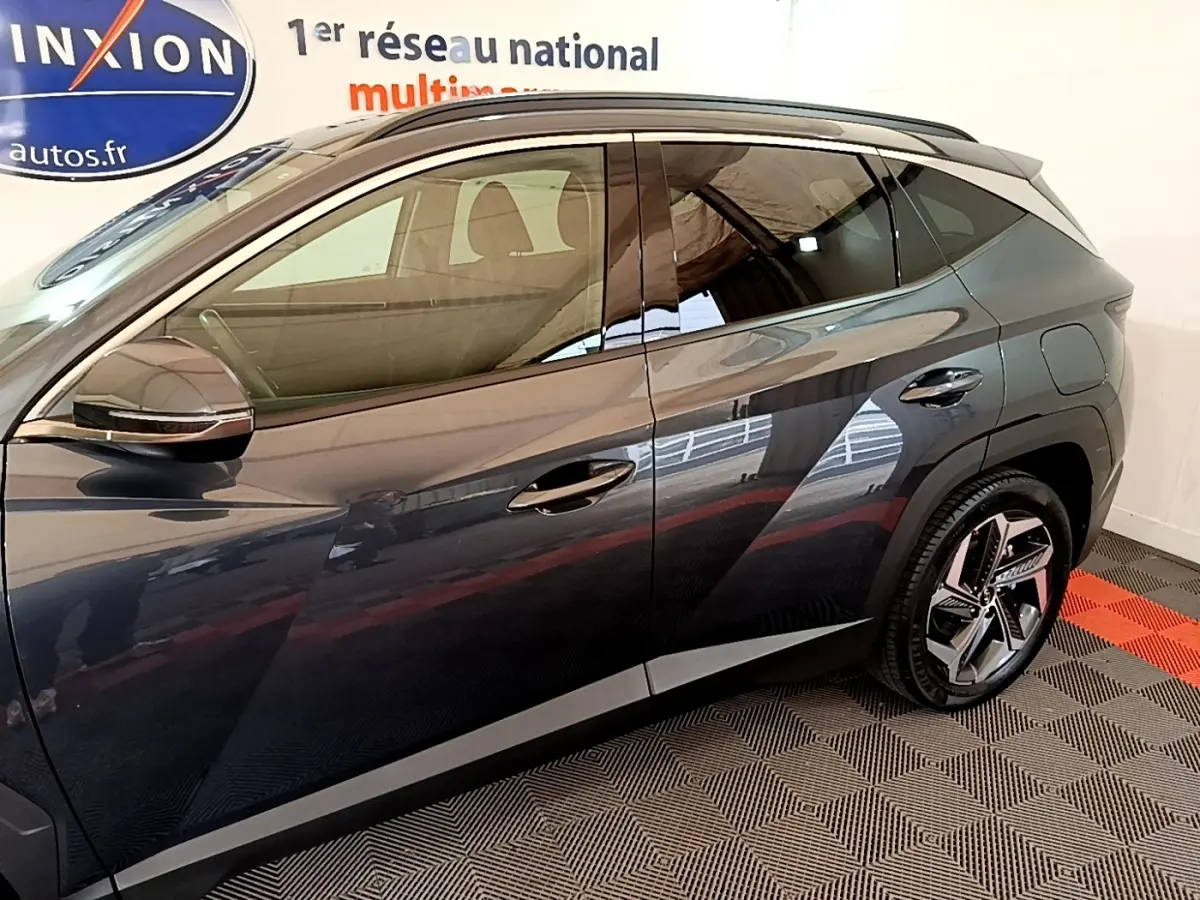 Vue côté gauche d’un Hyundai Tucson gris foncé 2022, mettant en valeur les jantes et la ligne de toit avec rails intégrés.