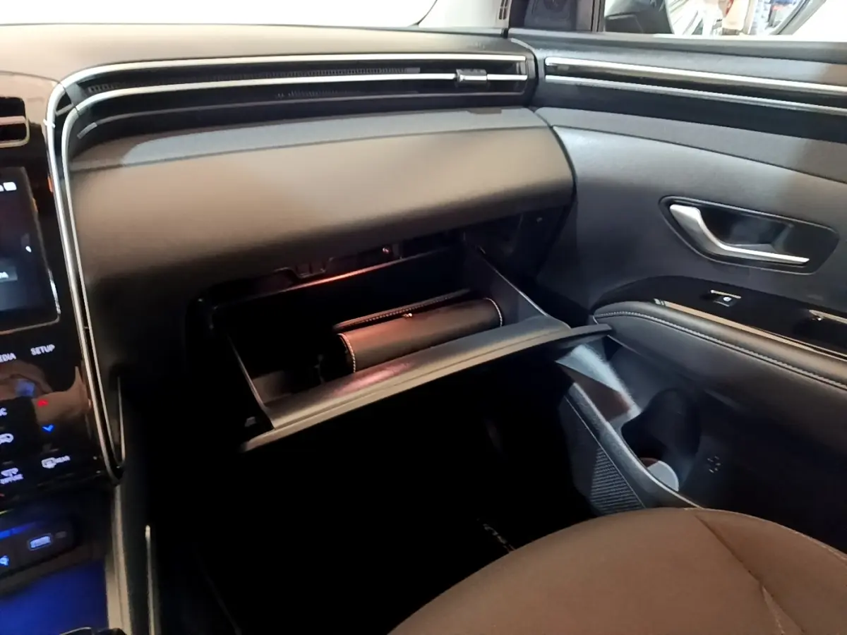 Intérieur Hyundai Tucson 2022 vue côté passager, boîte à gants ouverte, tableau de bord noir moderne avec écran tactile partiel visible.