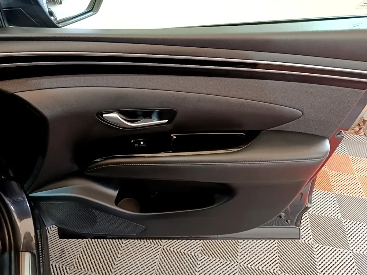 Vue rapprochée de la porte avant gauche du Hyundai Tucson gris foncé, avec garniture noire et poignée argentée.