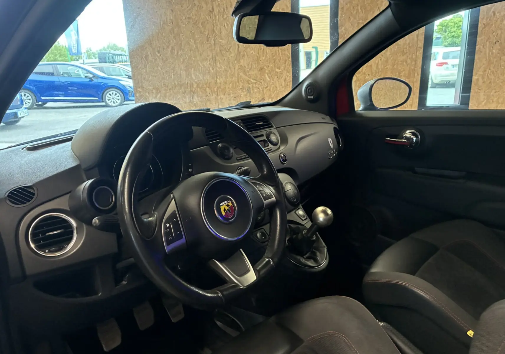 Vue intérieure côté conducteur de l'Abarth 500 Competizione 2016, volant sport, levier de vitesse manuel et sièges noirs.