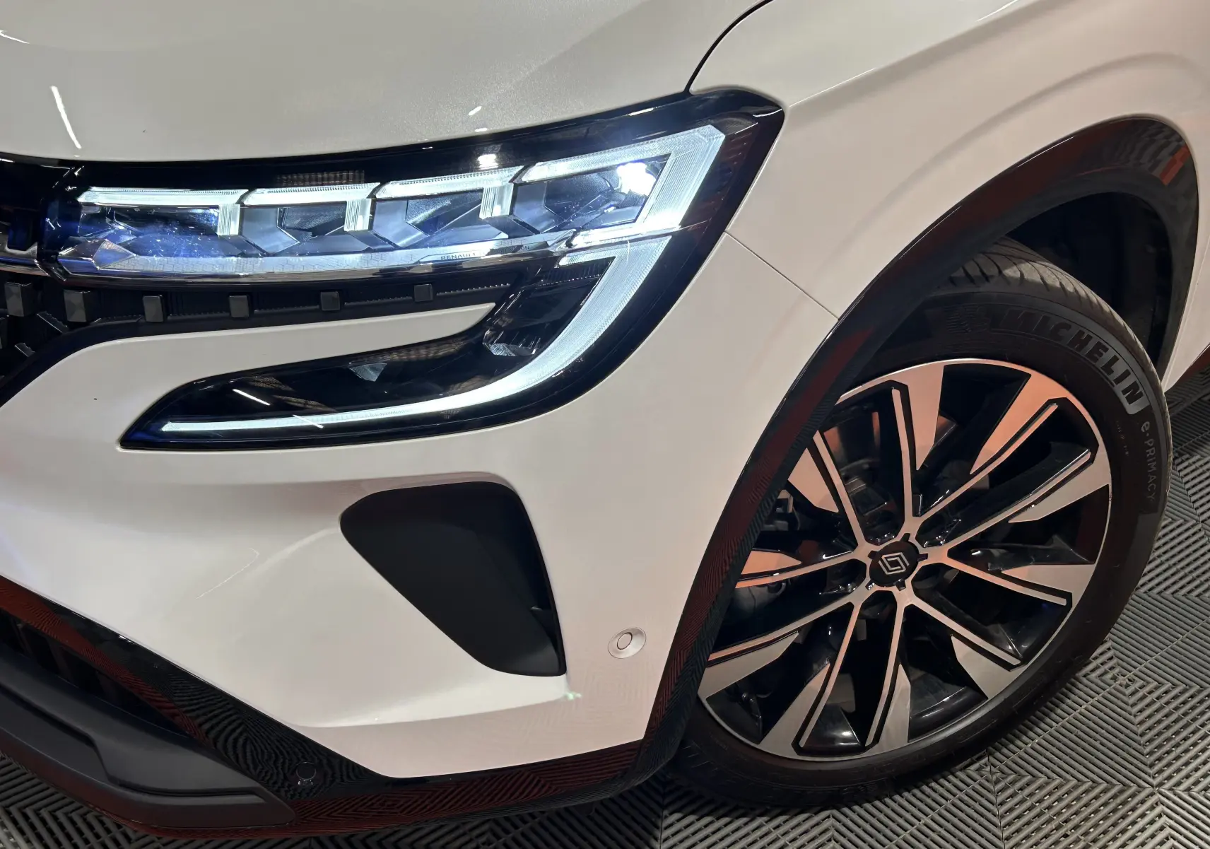 Gros plan sur l’avant droit blanc nacré du Renault Austral 2024 avec phares LED allumés et jante alliage noire et argent.