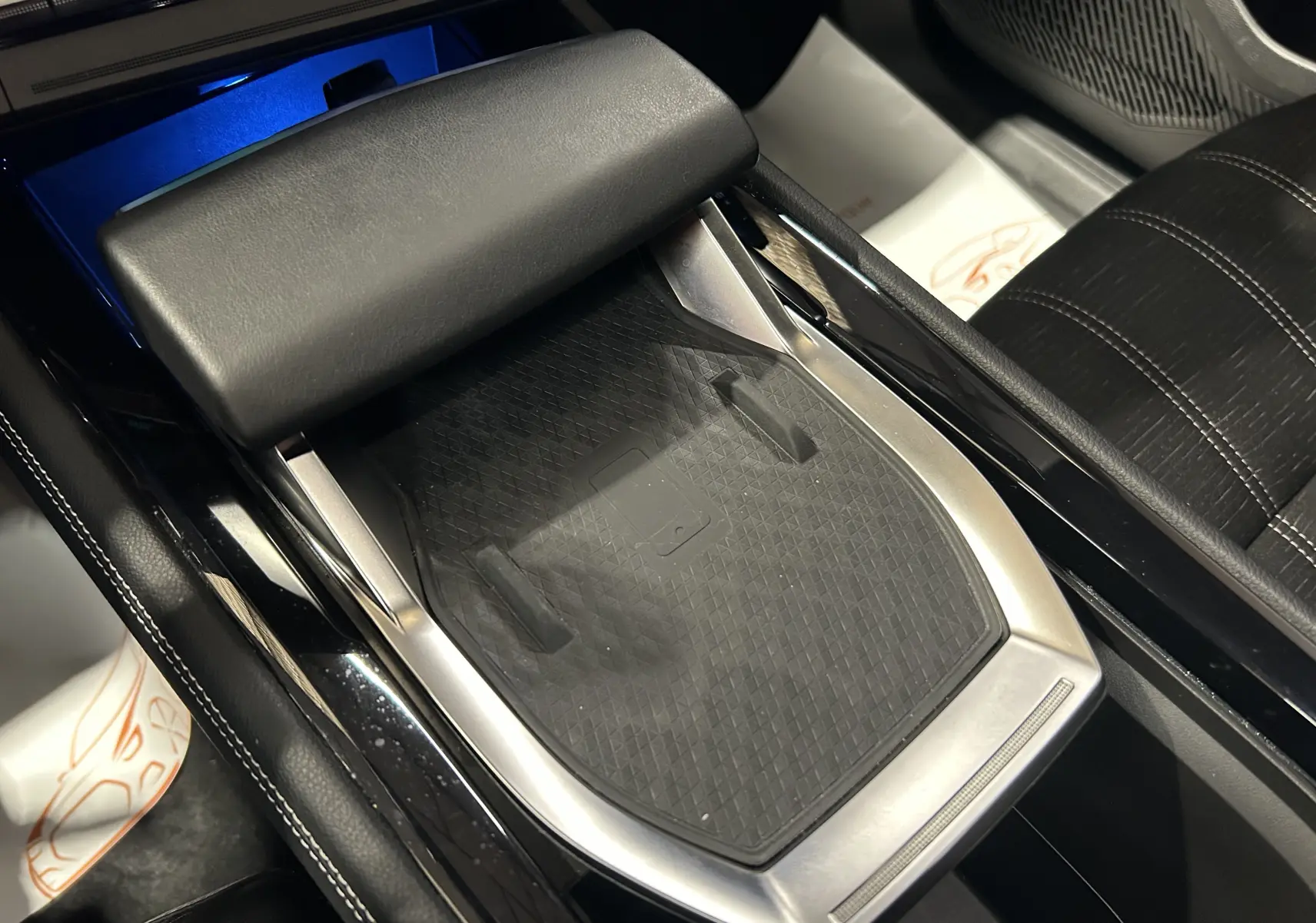 Vue rapprochée de la console centrale noire du Renault Austral 2024 avec accoudoir et surface de recharge sans fil.