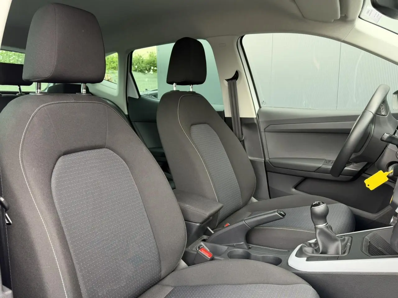 Vue intérieure avant du SEAT Arona 2025 TSI 115 Style, sièges tissu gris foncé avec boîte manuelle et accoudoir central.