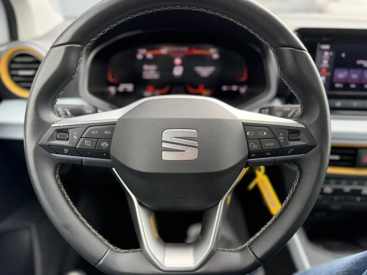 Vue rapprochée du volant noir du SEAT Arona 2025 avec commandes intégrées et tableau de bord digital en arrière-plan.
