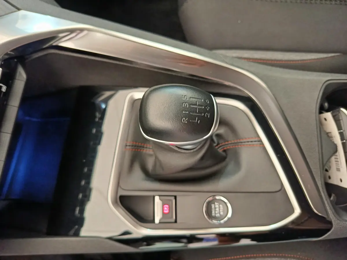 Gros plan sur le levier de vitesses manuel noir avec coutures rouges du Peugeot 3008 gris foncé, console centrale visible.