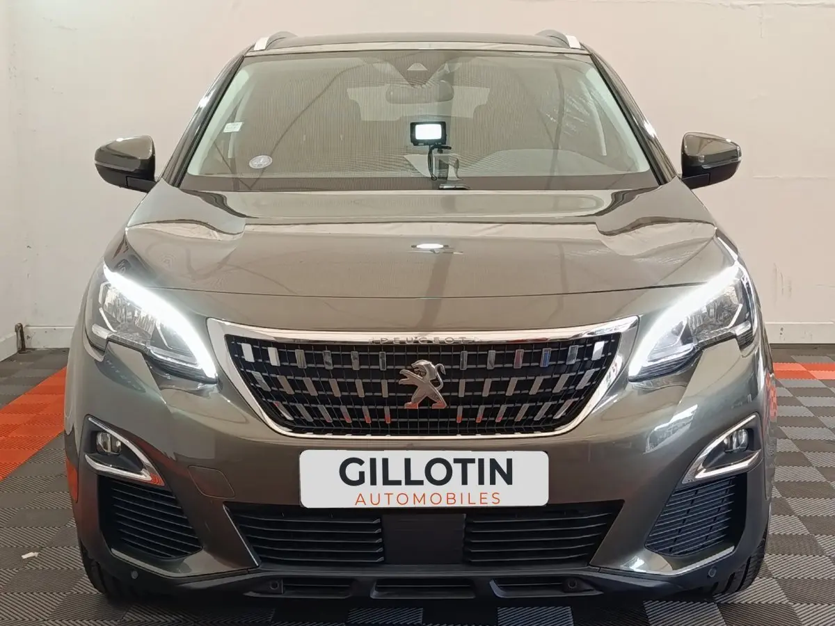 Vue frontale d'un Peugeot 3008 gris foncé avec phares LED allumés et calandre chromée distinctive.