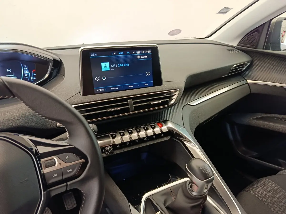 Intérieur du Peugeot 3008 2020, vue côté conducteur, tableau de bord noir avec écran tactile central et levier de vitesse manuel.