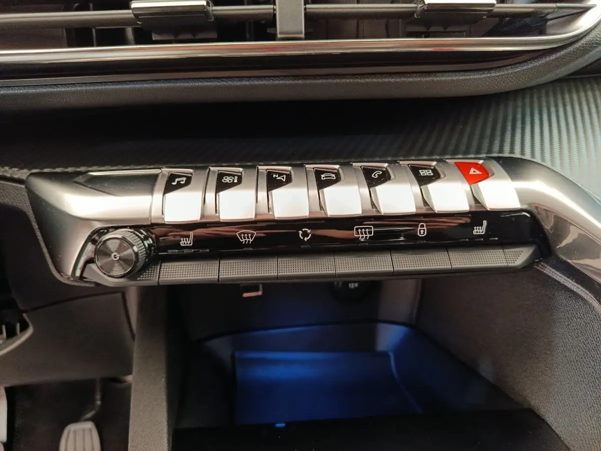 Gros plan sur la rangée de boutons argentés et noirs du tableau de bord du Peugeot 3008 gris foncé, avec commandes climatisation et hazard.