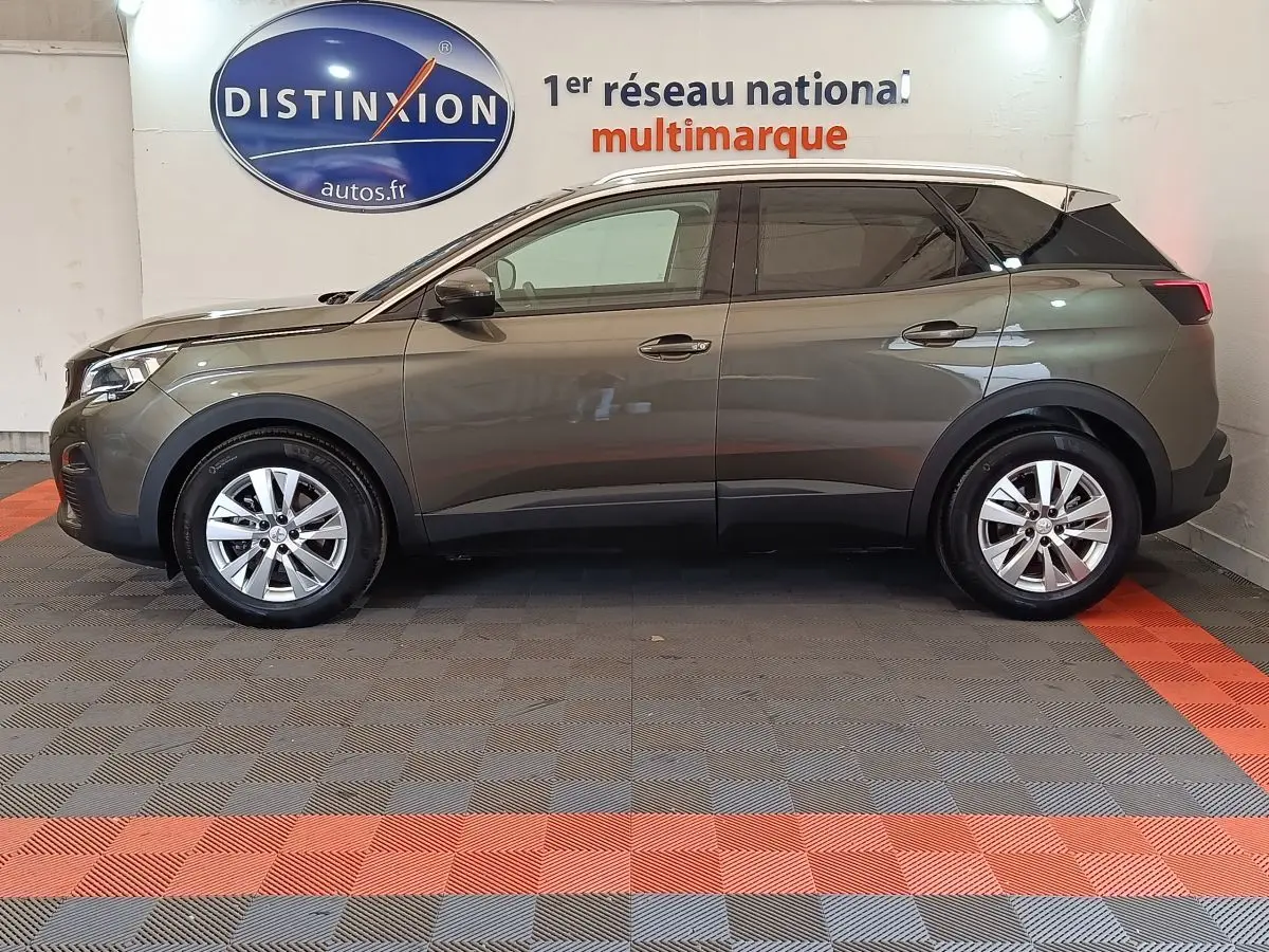 Profil côté gauche d'un Peugeot 3008 gris foncé 2020 garé en intérieur sur sol à damiers gris et orange.