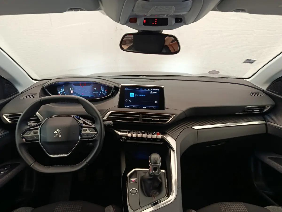 Vue intérieure frontale du tableau de bord et volant cuir noir du Peugeot 3008 gris foncé, avec écran tactile central allumé.