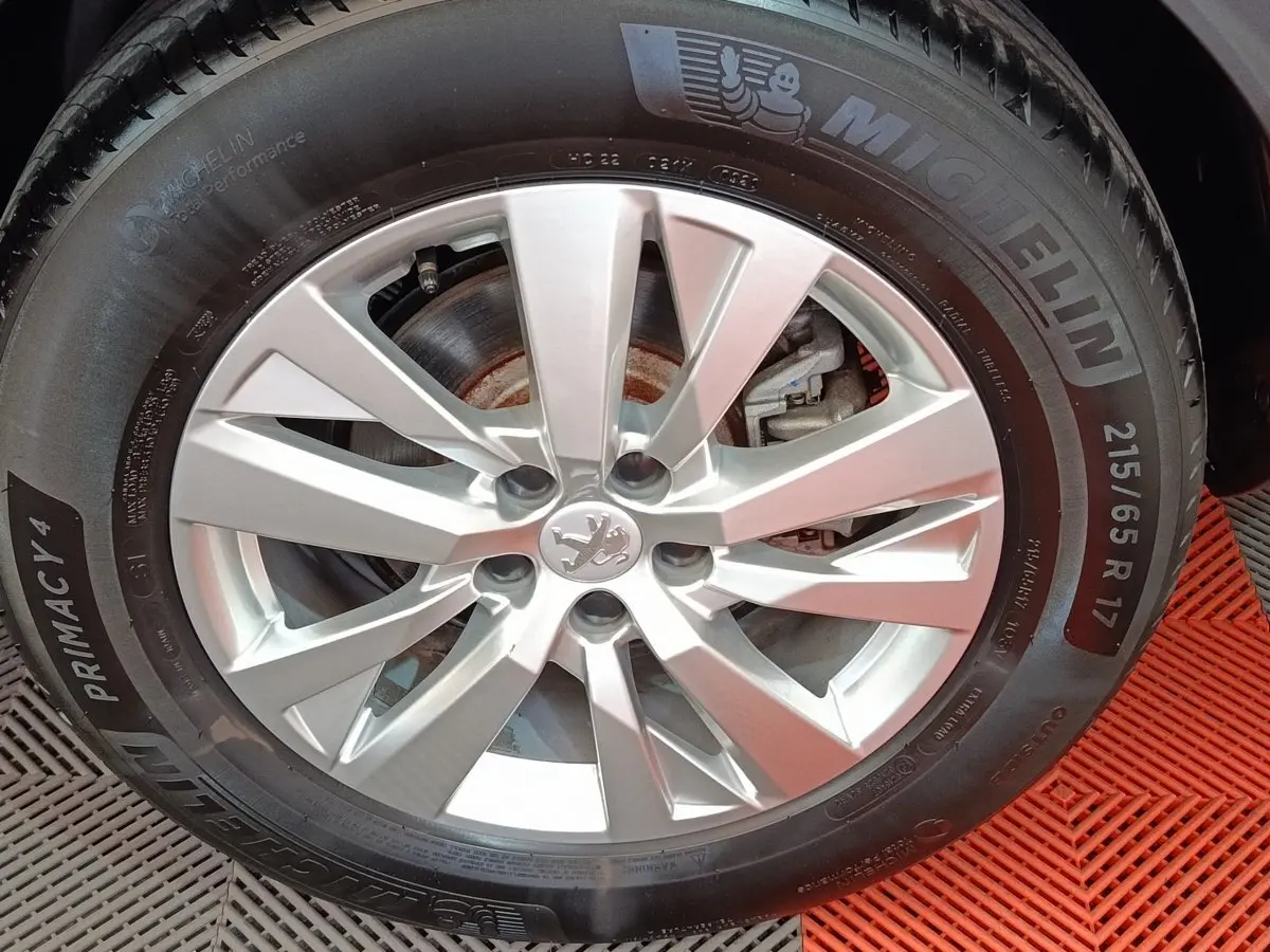 Gros plan sur la jante argentée avec logo Peugeot d'un 3008 gris foncé, pneu Michelin visible sur tapis rouge.