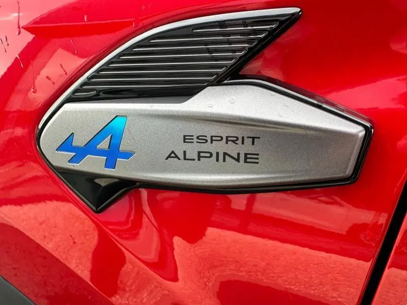 Gros plan sur l'insigne Esprit Alpine bleu et argent sur la carrosserie rouge flamme du Renault Captur hybride 2025.