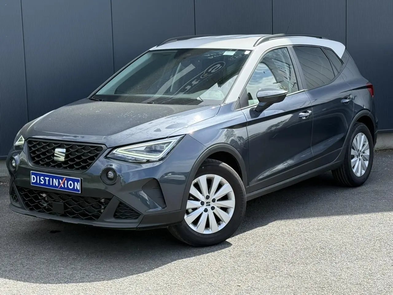 SEAT Arona TSI 115 Style 2025 en 3/4 avant droit, gris magnétique avec toit blanc contrasté et jantes alliage.