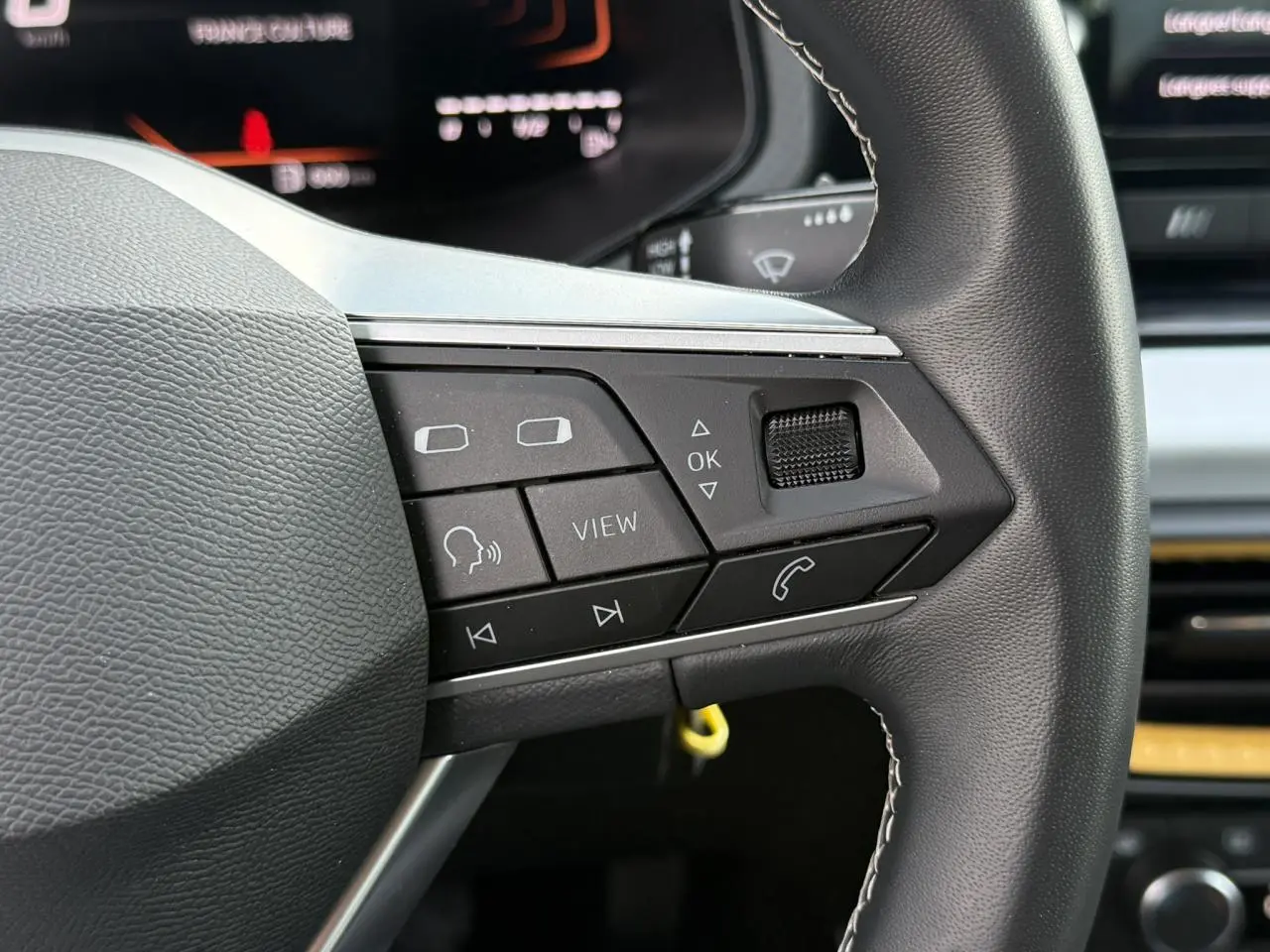 Gros plan sur les commandes au volant à gauche du SEAT Arona 2025, finition Style, avec tableau de bord digital en arrière-plan.