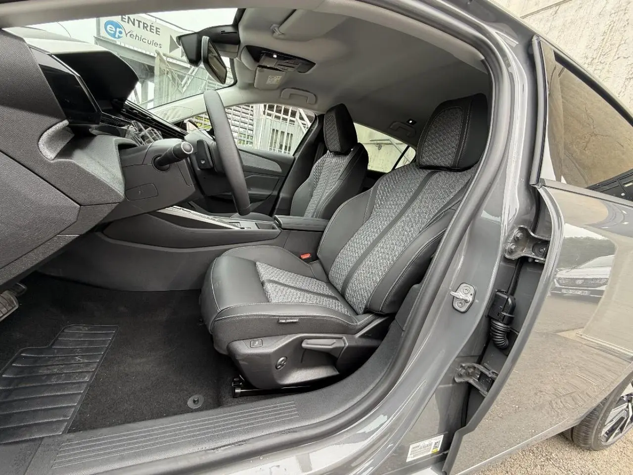 Vue intérieure côté conducteur de la Peugeot 308 gris sellenium, montrant les sièges en tissu et cuir avec surpiqûres contrastées.