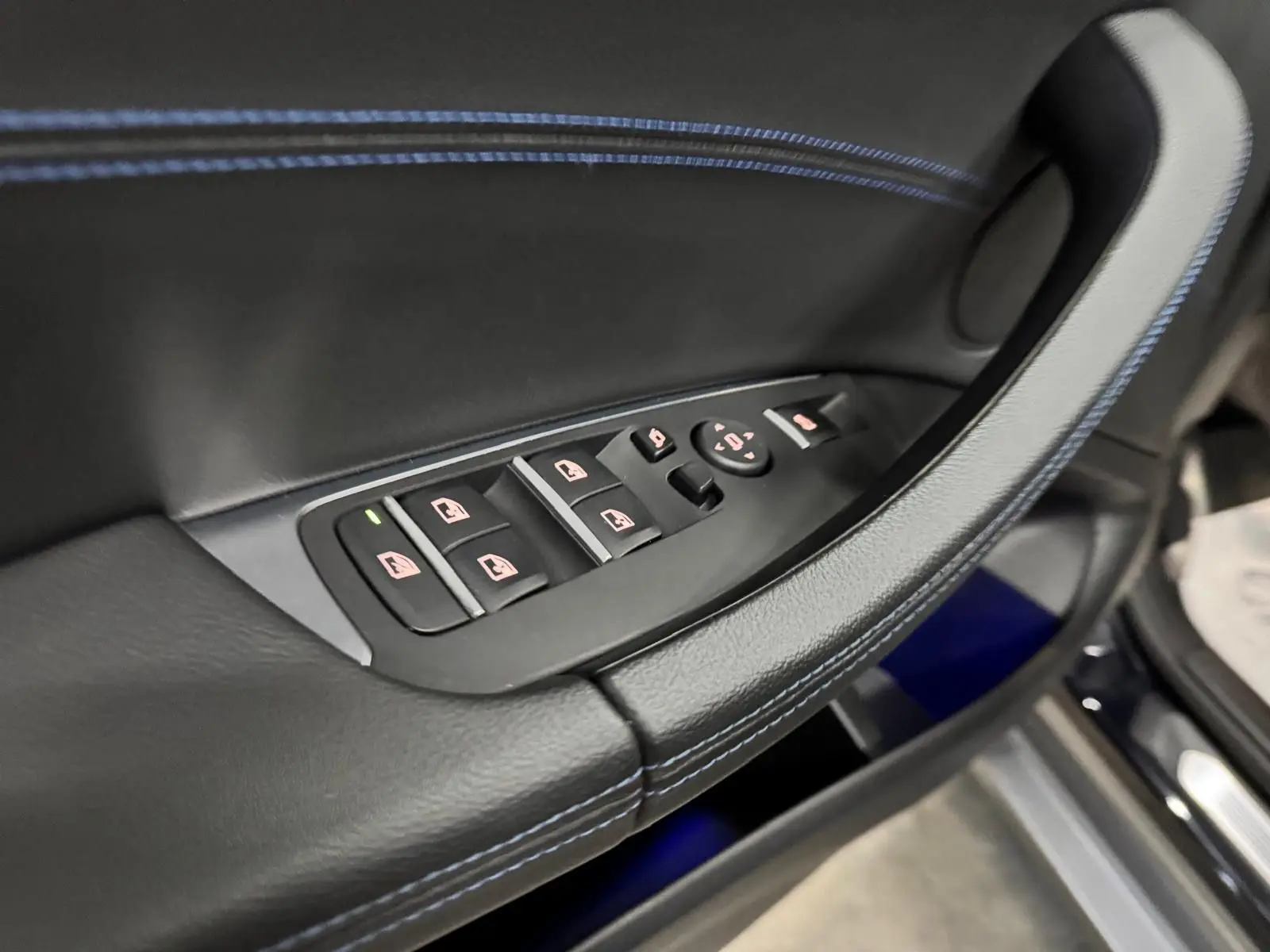 Gros plan sur la commande des vitres côté conducteur en cuir noir avec surpiqûres bleues dans une BMW X4 Carbonschwarz 2020.