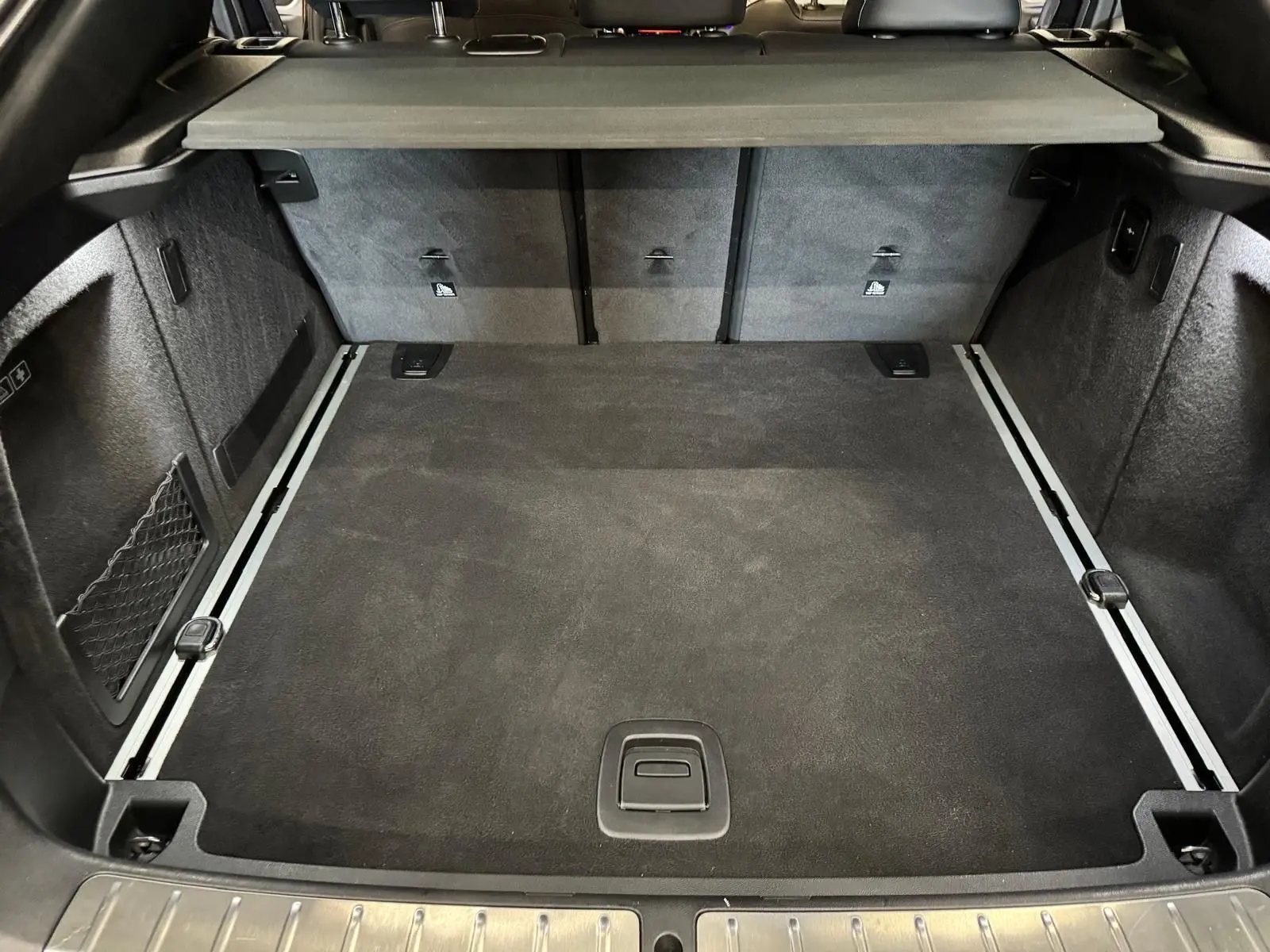 Coffre spacieux de BMW X4 XDrive 20d 2020 en Carbonschwarz, vue intérieure arrière avec revêtement noir et rails de fixation.