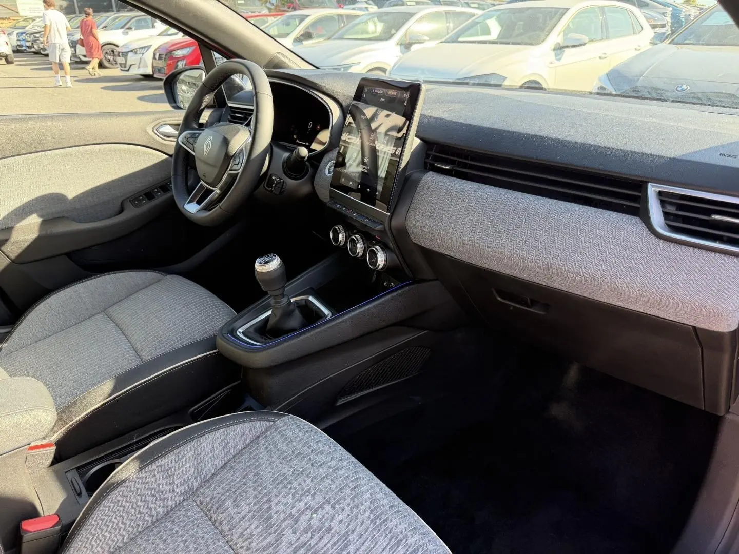 Intérieur avant droit de Renault Clio 2025, volant multifonction, sellerie grise, écran tactile vertical et boîte manuelle.