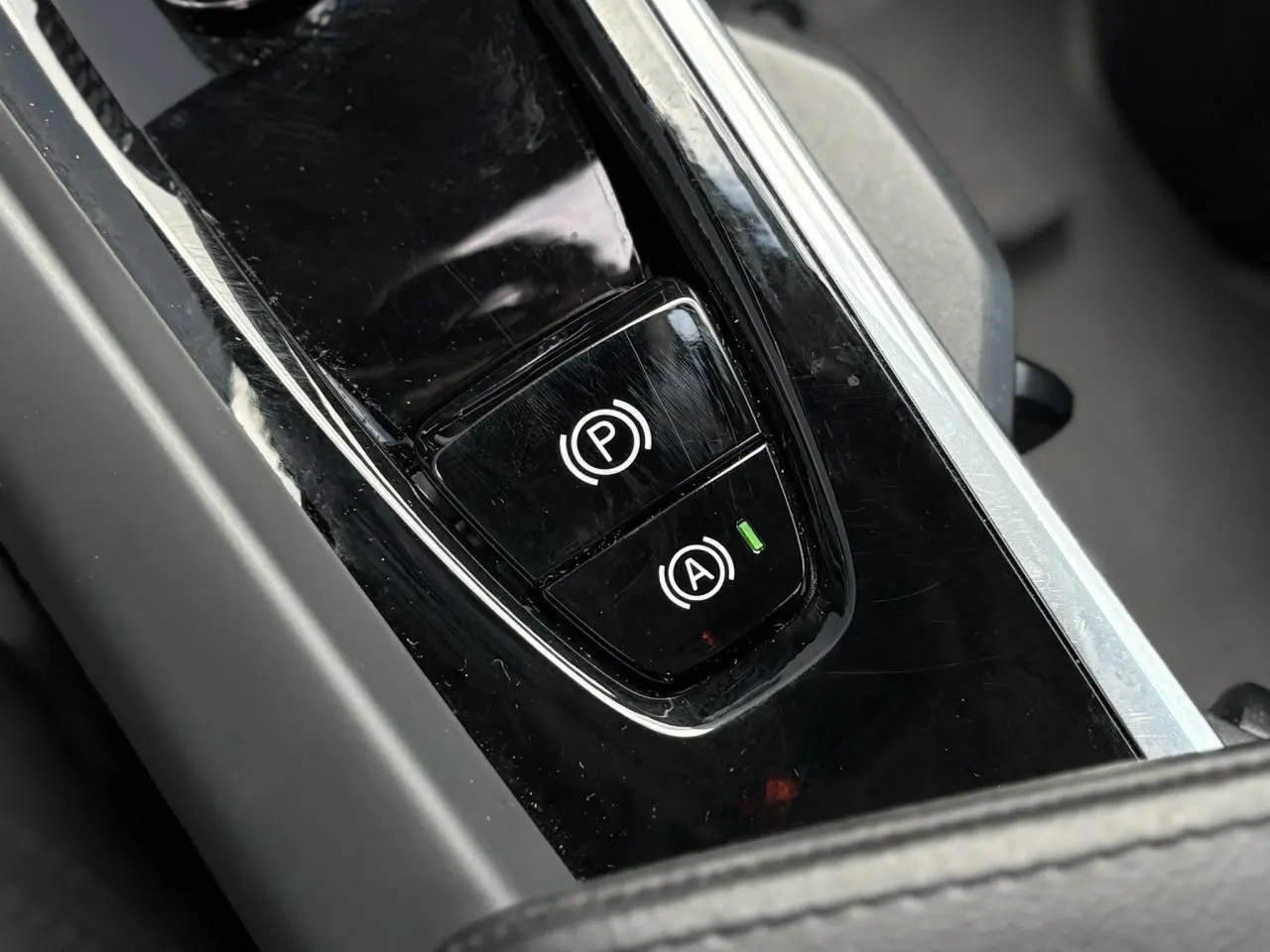 Gros plan sur les commandes du frein de parking et de l'arrêt automatique dans le console centrale noire du Volvo XC60 gris Silver 2024.