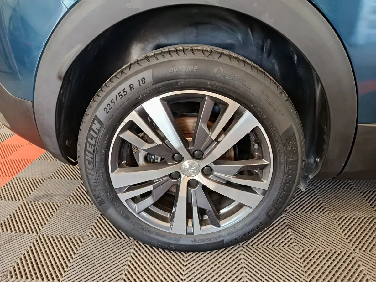 Gros plan sur la roue avant gauche d'une Peugeot 3008 bleu, jante alliage 18 pouces avec pneu Michelin.