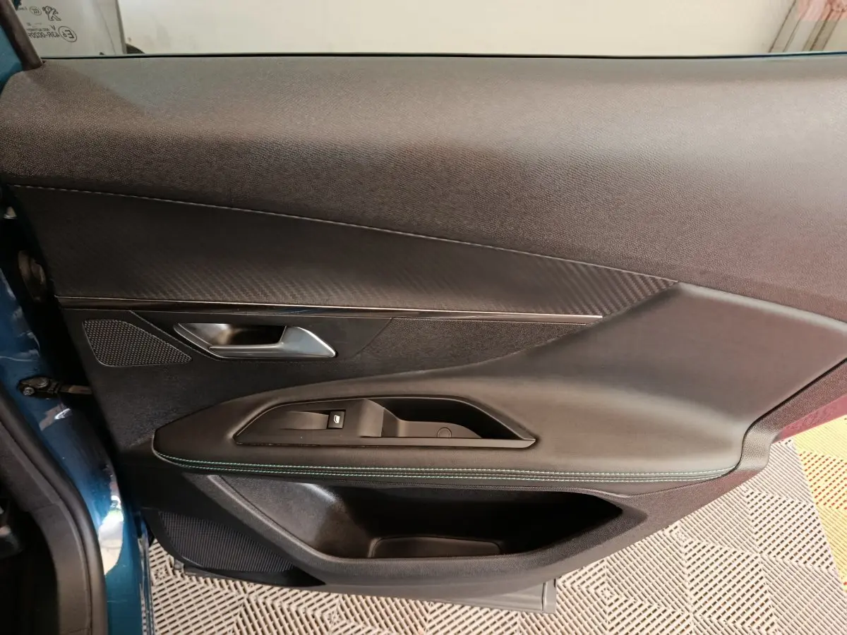 Gros plan sur la porte côté gauche du Peugeot 3008 bleu 2022, montrant la poignée, les commandes de fenêtre et la finition cuir avec surpiqûres vertes.