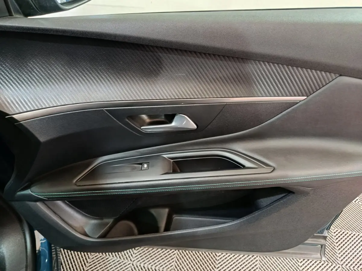 Gros plan sur la porte côté gauche du Peugeot 3008 bleu, avec garniture noire et insert effet carbone.