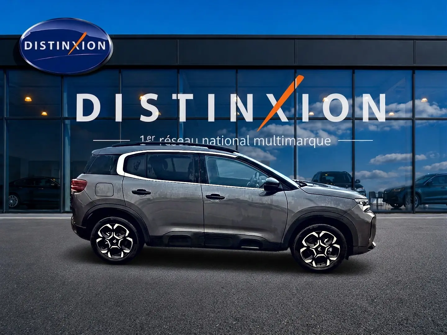 Profil côté gauche du Citroën C5 Aircross gris 2025, avec jantes alu et vitres arrière teintées, devant un showroom Distinxion.