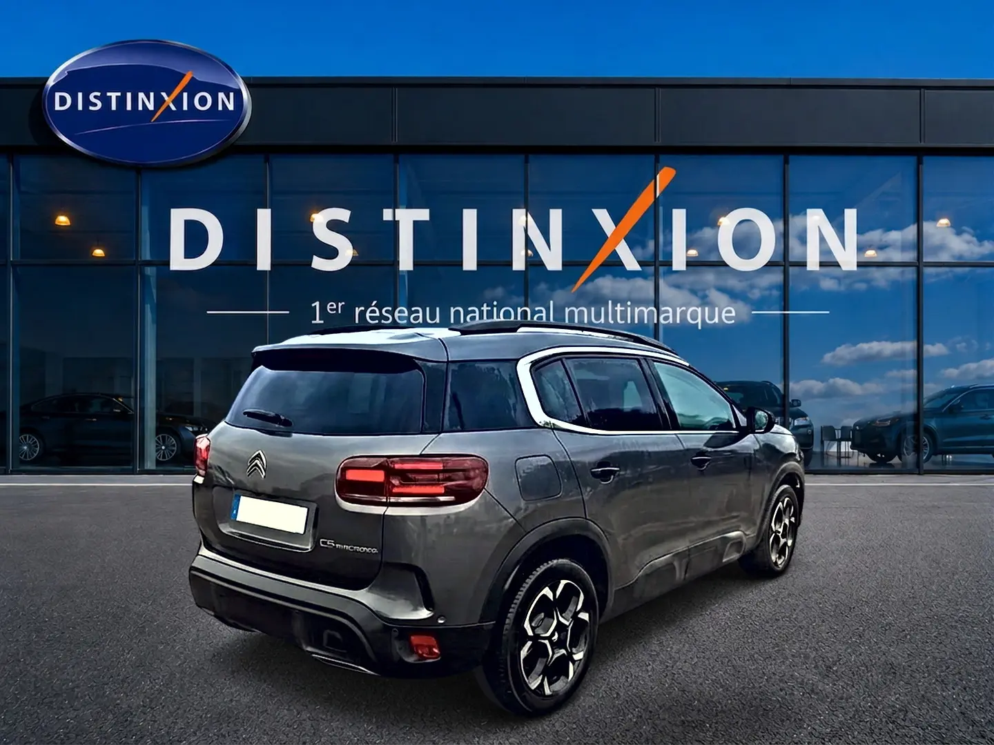 Vue 3/4 arrière droite du Citroën C5 Aircross gris 2025 avec jantes alu et barres de toit visibles.