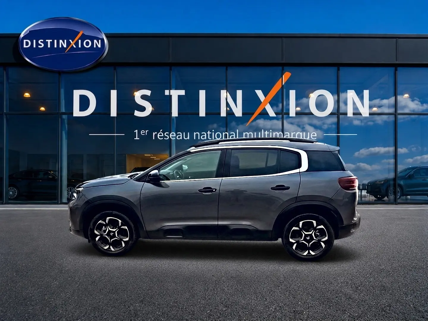 Profil côté gauche du Citroën C5 Aircross gris 2025 avec jantes alu et barres de toit visibles devant un showroom Distinxion.