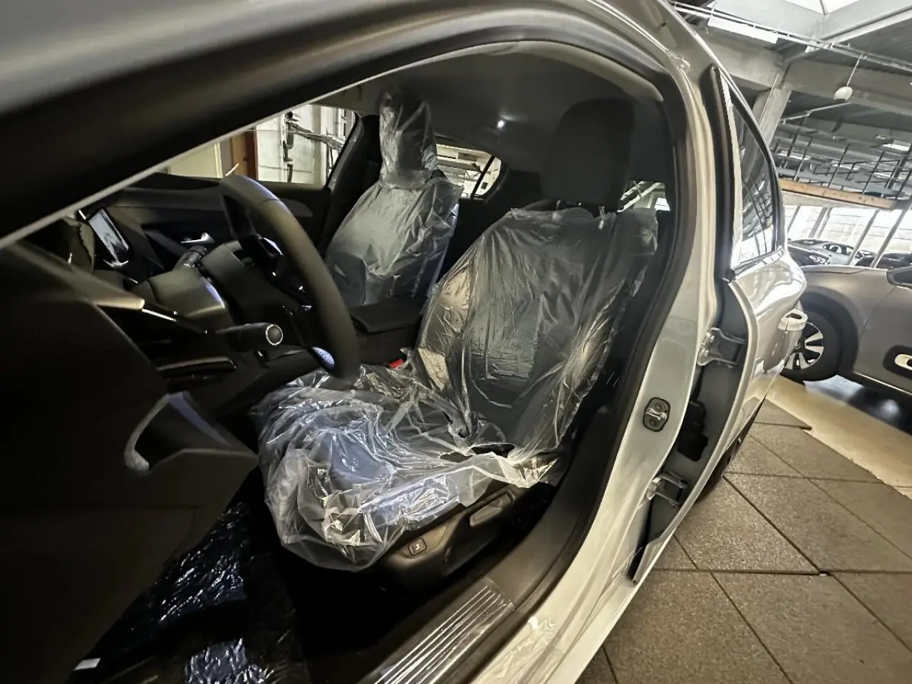 Intérieur de la Peugeot 308 blanc okenite 2024, vue côté conducteur avec sièges avant protégés par film plastique.