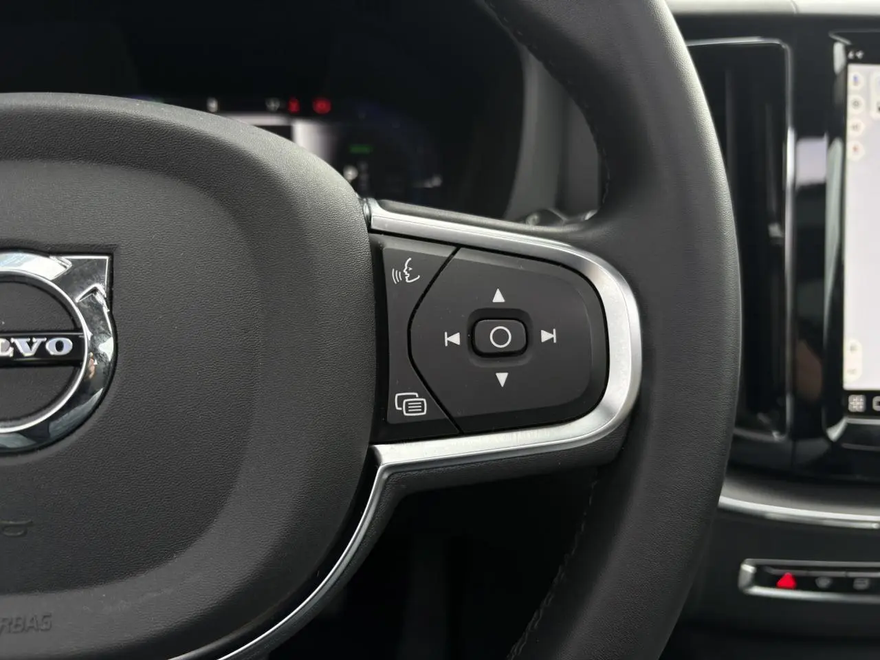 Gros plan sur le volant simili-cuir noir du Volvo XC60 2024 avec commandes audio et écran tactile visible à droite