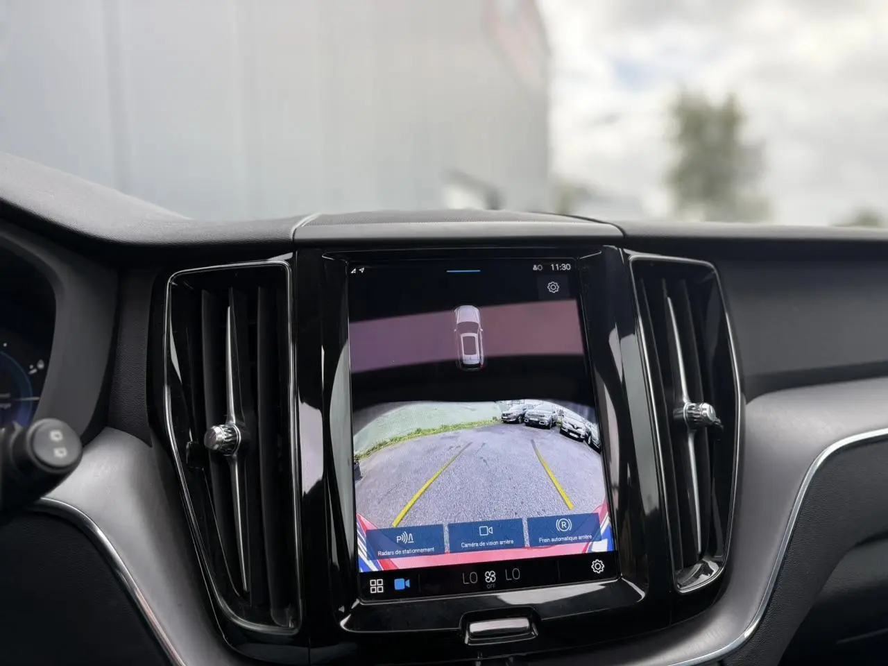 Écran tactile central affichant la caméra de recul du Volvo XC60 rouge fusion, intérieur noir avec aérateurs verticaux.